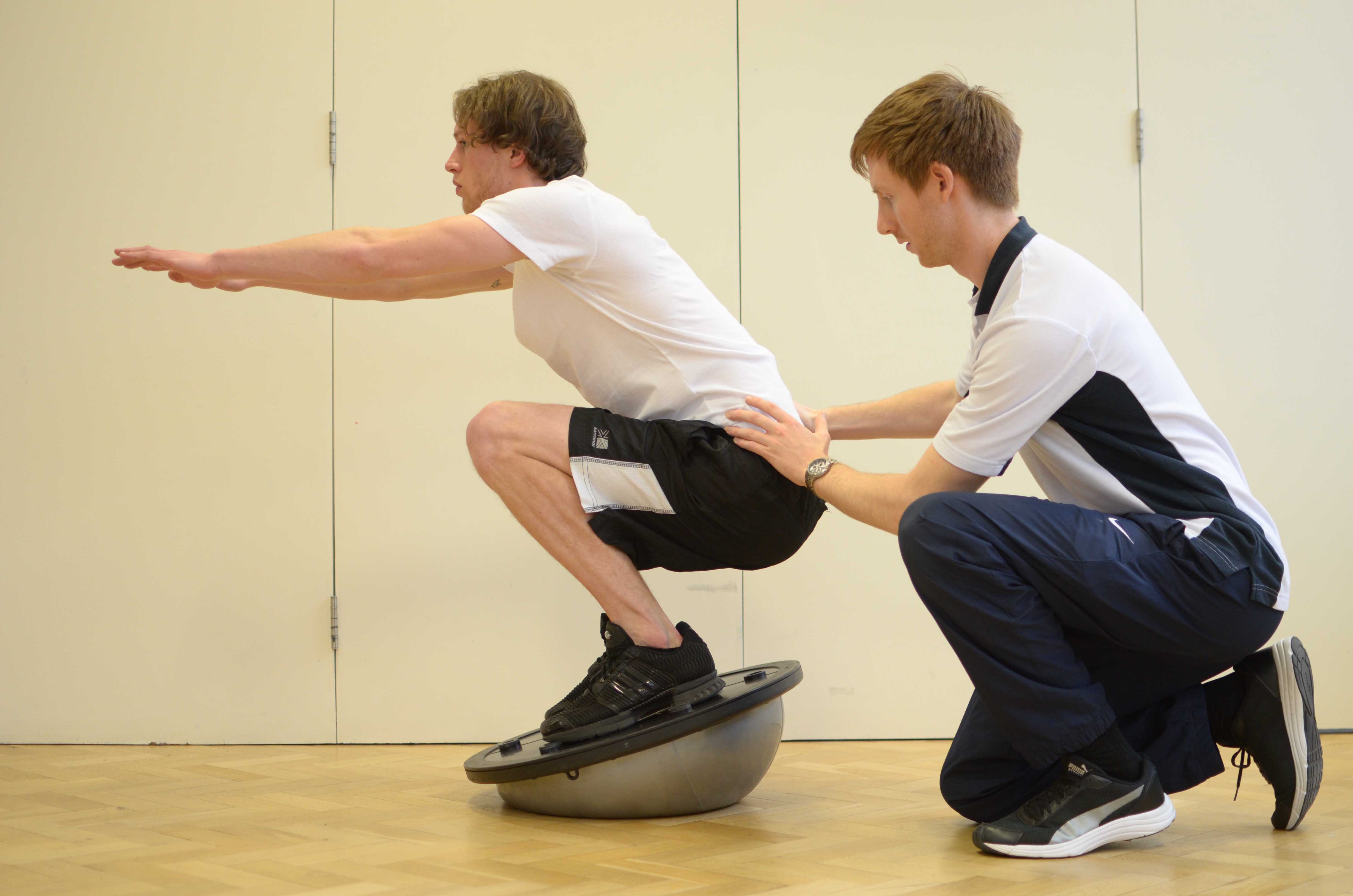 Leg strengthening and stability exercises using squats on a balance board under supervision of specialist MSK physiotherapist Leg strengthening and stability exercises using squats on a balance board under supervision of specialist MSK physiotherapist