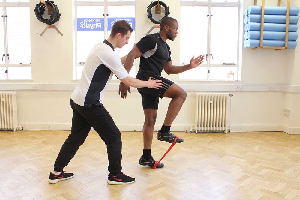 Physiotherapist supervising lower limb exercises using a resistance band. Physiotherapist supervising lower limb exercises using a resistance band.